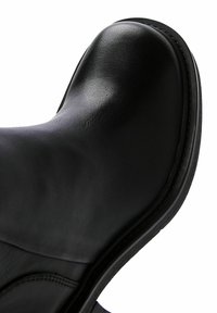 Black leather boot highlighting a smooth, rounded toe, sleek design, and a textured finish. Features minimal stitching and a durable sole.