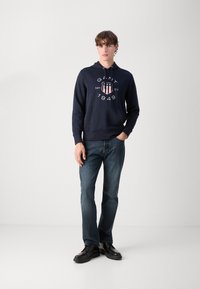 Sudadera de algodón azul marino con un bolsillo canguro en la parte delantera y estampado gráfico. Combinada con jeans de mezclilla azul oscuro y zapatos negros con cordones.