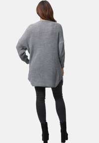 Szary, oversize'owy sweter z dzianiny o luźnym kroju, z opadającymi ramionami i bocznymi rozcięciami, zestawiony z czarnymi wąskimi dżinsami i botkami za kostkę.