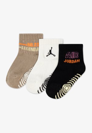 Trois chaussettes pour enfants montant à la cheville, en marron, blanc et noir, avec des logos de la marque Jordan et des motifs antidérapants sous les semelles.