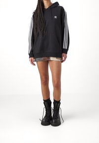 Svart hoodie med vita vertikala ränder på ärmarna, kenguruficka, kombinerad med jeansshorts och kraftiga svarta kängor.