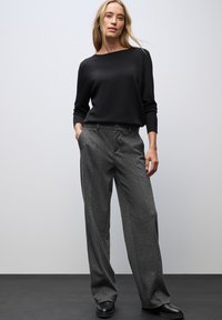 Suéter negro de manga larga y pantalones de pierna ancha gris con rayas. Los pantalones tienen un cierre de botón y bolsillos frontales. Calzado plano negro.