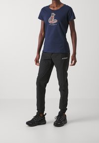 Granatowy t-shirt z grafiką niedźwiedzia, zestawiony z czarnymi lekkimi spodniami oraz czarnymi butami trekkingowymi z teksturowaną podeszwą i elastycznymi mankietami.