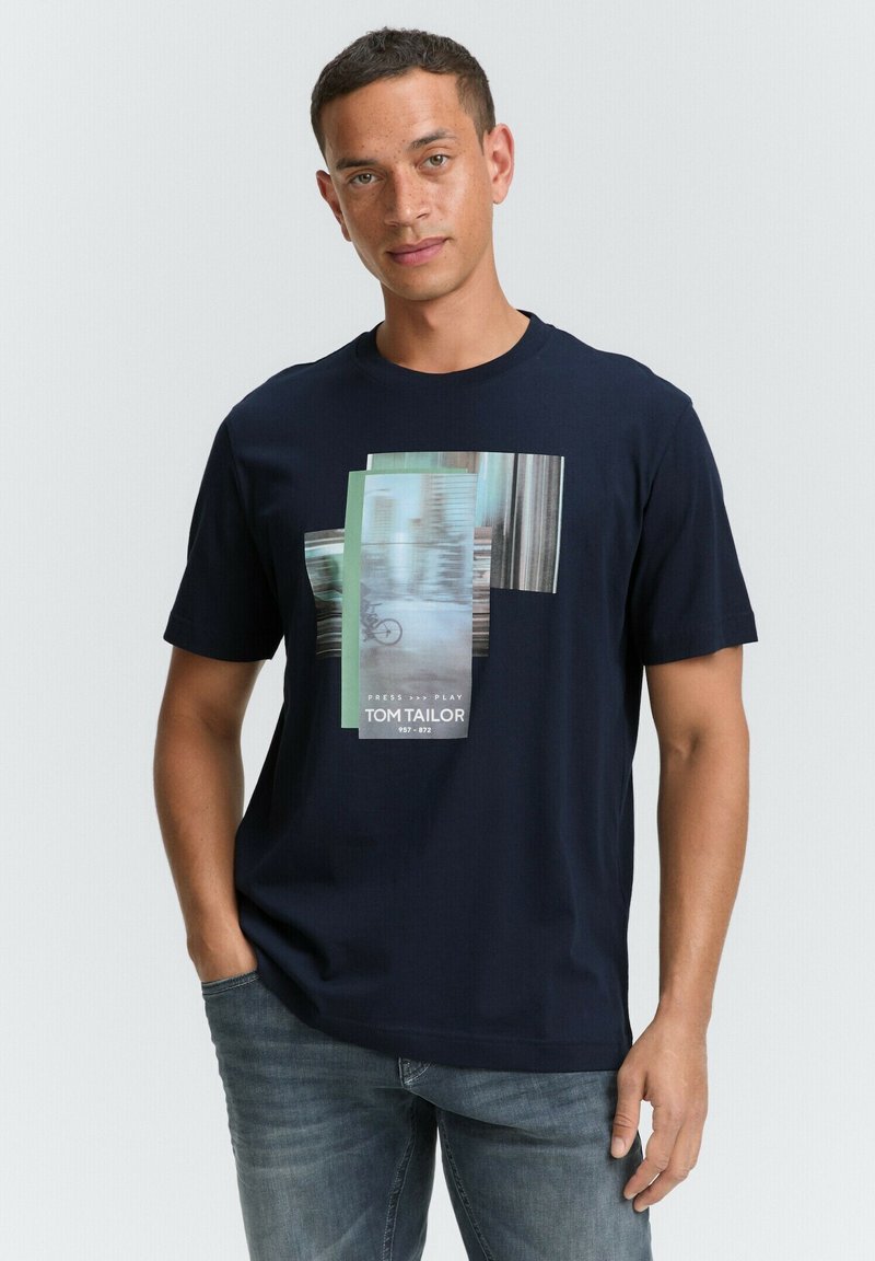Tricou din bumbac bleu marin, cu un design grafic stratificat în verde și gri, având textul "APASĂ >>> REDARE TOM TAILOR" în centru.