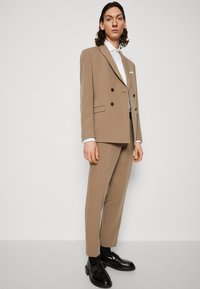 Bežna dvoredna obleka s črnimi gumbi. Bele srajce spodaj. Črne usnjene čevlje. Slim fit hlače, minimalne podrobnosti. Enobarvna ozadje.