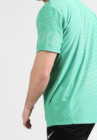 Camiseta de Nike verde de manga corta, con un patrón texturizado y un gran logo en el lado. Tejido suave con un corte relajado.
