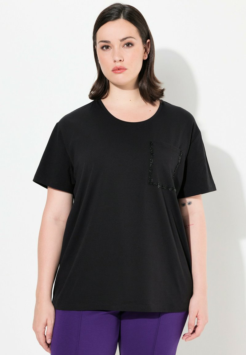 Musta t-paita lyhyillä hihoilla, pyöreällä kaula-aukolla ja vasemmalla puolella mustilla paljeteilla koristeltu tasku. Pehme ä, sileä kangas.