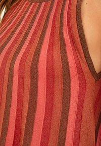 Haut tricoté à rayures rouges et brunes, sans manches, avec un tricot côtelé texturé, présentant des rayures de largeurs variées pour un intérêt visuel.