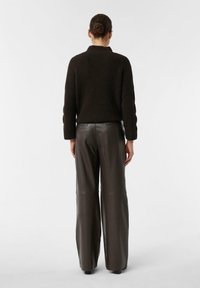 Dark brown ribbed sweater paired with high-waisted dark leather trousers. The outfit features a relaxed fit and textured fabric.