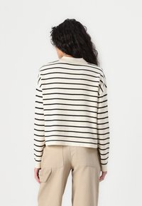 Cropped sweater in cream with black horizontal stripes. Features a round neckline and long sleeves. Soft texture, casual design.