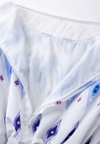 White fabric with a geometric pattern in blue and purple. Features a zip closure and a gathered neckline. Smooth texture.