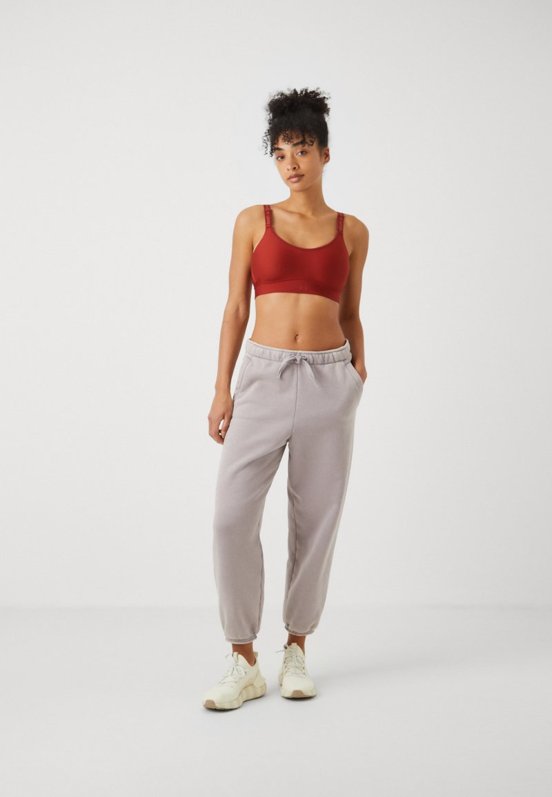 Roter Sport-BH mit verstellbaren Trägern, kombiniert mit hellgrauen Jogginghosen mit elastischem Bund und Seitentaschen. Weiße Sneakers.