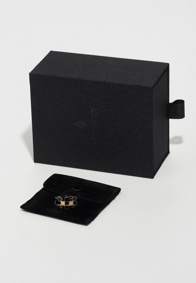 Black textured jewelry box with lid, featuring a black suede pouch containing a metallic ring with gold accents and geometric design.