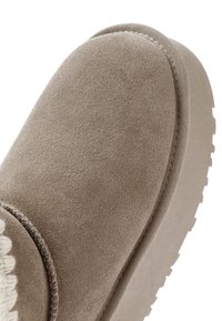 Beige suède enkellaars met een textuurlagen oppervlak, ronde neus en rubberen zool. Heeft een gestikte naad langs de bovenkant en een ribbeldetail.