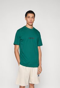 Zelené bavlnené tričko s okrúhlym v�ýstrihom a krátkymi rukávmi, na hrudi čierne logo „adidas“. Jednoduchý dizajn, voľný strih.