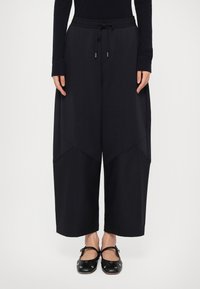 Wijdvallende, zwarte joggingbroek met een elastische tailleband, trekkoord en contrasterende stofpanelen. Zachte textuur, ontspannen pasvorm en minimale afwerking.