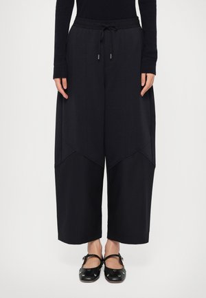 Wide-leg, black sweatpants with an elastic waistband, drawstring, and contrasting fabric panels. Smooth texture, relaxed fit, and minimal detailing.