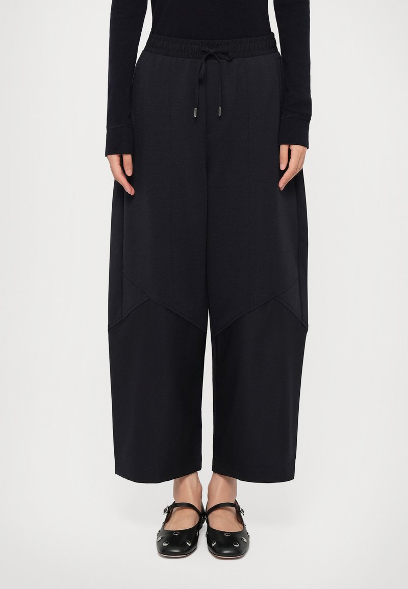 Wijdvallende, zwarte joggingbroek met een elastische tailleband, trekkoord en contrasterende stofpanelen. Zachte textuur, ontspannen pasvorm en minimale afwerking.