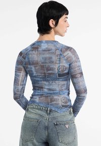 Langsleeve, doorschijnende top met een collage van vintage tankstationlogo's in blauwtonen. Gepaarde met hoge taille, vervaagde denim jeans.
