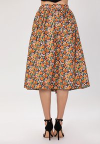 Jupe midi florale noire, ornée de fleurs orange, violettes et vertes. Taille élastique et tissu fluide ; associée à des talons aiguilles noirs.