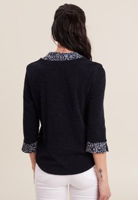 Pullover navy con maniche a tre quarti e polsini a fantasia. Tessuto testurizzato, orlo arrotondato e scollatura con colletto.