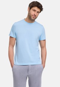 Jasnoniebieska bawełniana koszulka z okrągłym dekoltem, krótkimi rękawami i gładką fakturą. Dopasowany krój, noszona na szarych, textured spodniach.