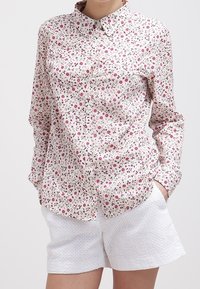 Blommig skjorta med knappar i vitt med rosa och gröna mönster, med klassisk krage och långa ärmar. Matchad med strukturerade vita shorts.