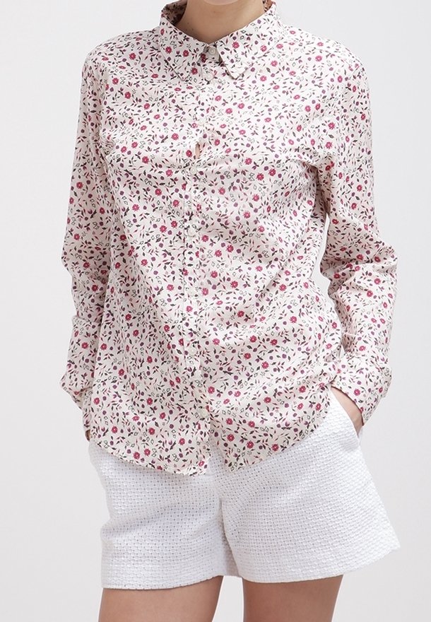 Blommig skjorta med knappar i vitt med rosa och gröna mönster, med klassisk krage och långa ärmar. Matchad med strukturerade vita shorts.