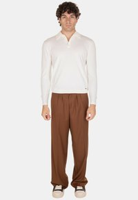 Camicia polo bianca a maniche lunghe con colletto, abbinata a pantaloni larghi marroni e sneakers nere con suola bianca. Design semplice e pulito.
