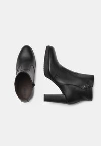 Bottines noires en cuir avec un bout arrondi, talon bloc et fermeture éclair sur le côté. Présentent des détails de couture minimalistes et des accents de matériel décoratif.