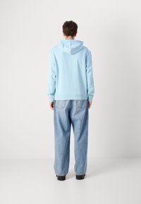 Sudadera azul clara con capucha ajustable, textura suave y puños acanalados, combinada con jeans azul claros de corte holgado, y zapatos negros.