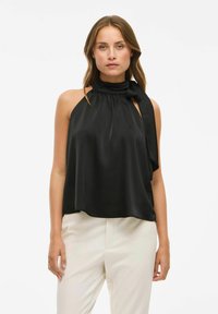 Mustmust värvi halter-top, millel on drapeeritud disain, kaela juures lipsuga kinni sidumise võimalus ja A-linjaliik. Sile tekstuur ja mugav lõige.