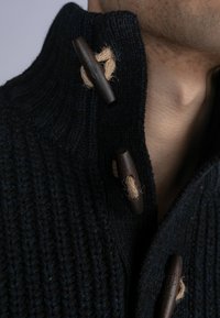 Pulover tricotat de culoare bleumarin, cu guler înalt, având închideri din toggles de lemn și accente din sfoară, evidențiind un model texturat, cu dungi.