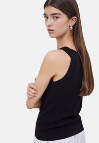 Top negro sin mangas con un diseño ajustado, acentos acanalados en los hombros y una textura suave. Modelo lleva un anillo de plata y pendientes.