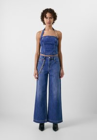 Denim crop top med halterneck-design, parret med brede jeans. Begge i mellem blå, med guld kædedetaljer på jeans.
