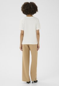T-shirt blanc à manches courtes associé à un pantalon large beige. Le tissu paraît lisse avec une coupe décontractée et un col rond.