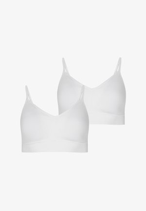 Modelka nosi biały biustonosz typu bralette i jasnobrązowy kardigan, zestawione z wysokim stanem i prostymi nogawkami w niebieskich dżinsach. Bez butów. Gładkie tekstury tkanin.