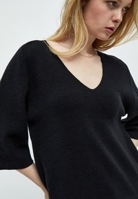 Maglione nero oversize con scollatura a V profonda, maniche a 3/4 e una texture morbida. Design semplice senza motivi o dettagli visibili.