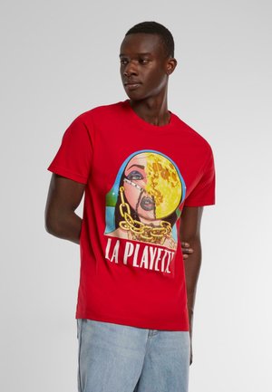 Red cotton t-shirt featuring a graphic design of a woman's face with gold accents and the text "LA PLAYETTE" below. Short sleeves, crew neck.
