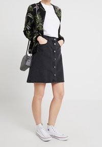 Černá džínová sukně s předními knoflíky a kapsami, spárovaná s bílým tričkem a vzorovanou černou bomber bundou. Bílé vysoké tenisky.