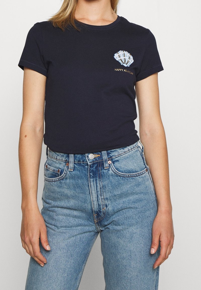 Námořnické bavlněné tričko s krátkými rukávy a přiléhavým střihem. Obsahuje grafiku mušle a výšivku "ŠŤASTNÝ JAKO MINHA" ve zlaté barvě.