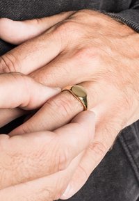 Gouden ring met een glad, afgerond ontwerp zit op een vinger, met handen in de nabijheid, waarbij de huidtextuur en subtiele details worden getoond.