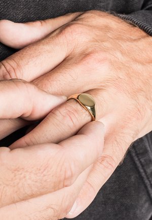 Gold ring with a smooth, rounded design sits on a finger, with hands in close proximity, showing skin texture and subtle details.