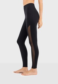 Leggings noirs taille haute avec des panneaux latéraux transparents, une texture lisse et un design ajusté pour le confort et la flexibilité.