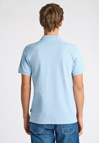 Polo shirt azzurro chiaro con maniche corte, colletto a coste e etichetta all'orlo. Indossato con jeans in denim, che mostrano una vestibilità comoda.