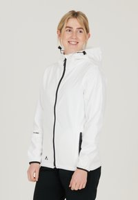 Vit vattentät jacka med dragkedja framtill, justerbar huva, elastiska ärmslut, sidofickor med dragkedja och svarta detaljer vid dragkedjorna och loggan.