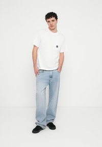 Biała bawełniana koszulka z krótkimi rękawami i kieszenią na piersi; w zestawieniu z jasnoniebieskimi dżinsami; czarne obuwie. Prosty i casualowy design.