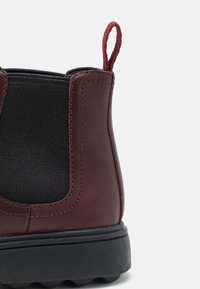 Burgundy läderankelboots med elastiska sidopaneler och en dragflik. Har en gummisula med texturerad yta och sömnadsdetaljer.