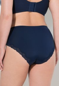 Slip alta blu navy con bordi in pizzo scallop, realizzata in morbido tessuto per garantire comfort.