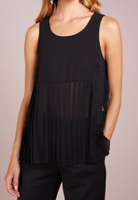 Svart ärmlös topp med en texturerad plisserad design vid nederkanten, med en slät övre del och diskreta sidofickor.